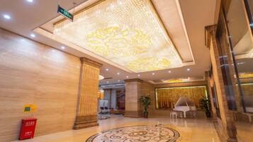 A hotel lobby with a patterned carpet, a chandelier, and a reception desk.