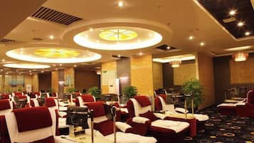 A hotel conference room with multiple tables and chairs, large circular ceiling lights, and a carpeted floor.