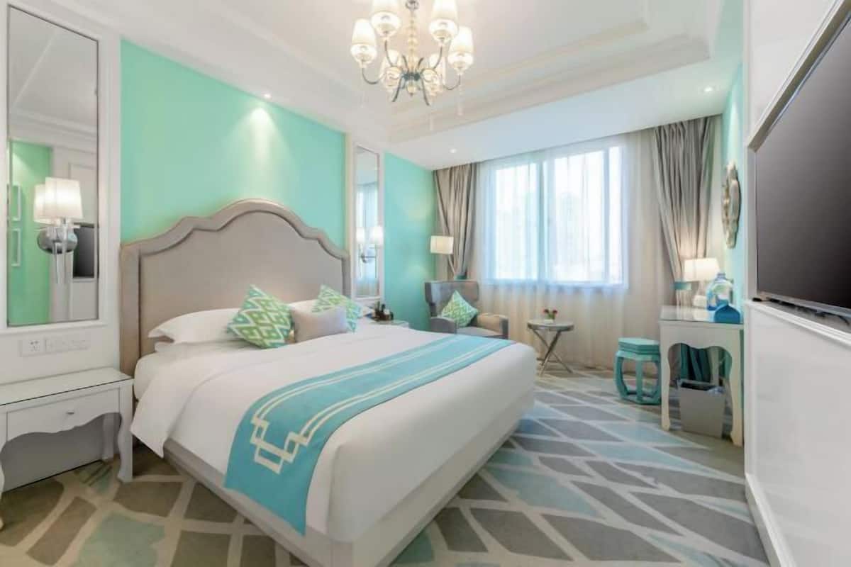 A hotel room with a large bed, a chandelier, a TV, and a window with curtains.