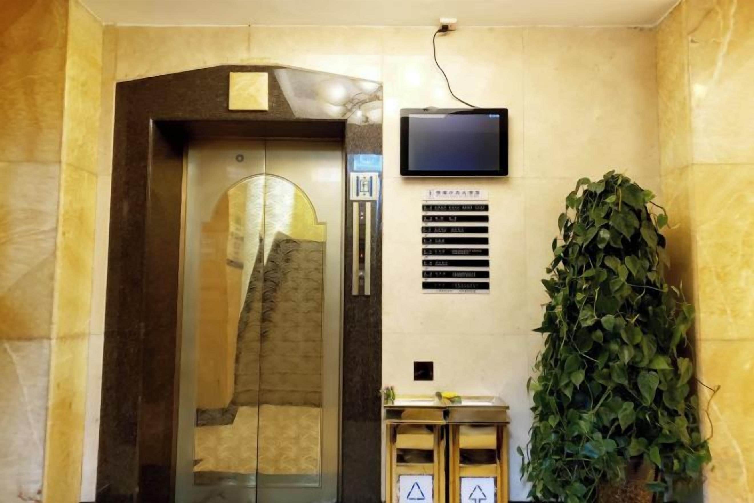 Un ascensor con pantalla digital, una planta en maceta y un cartel de seguridad.