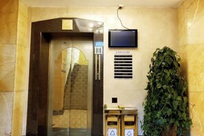 Un ascenseur doté d’un écran numérique, d’une plante en pot et d’un panneau de sécurité.