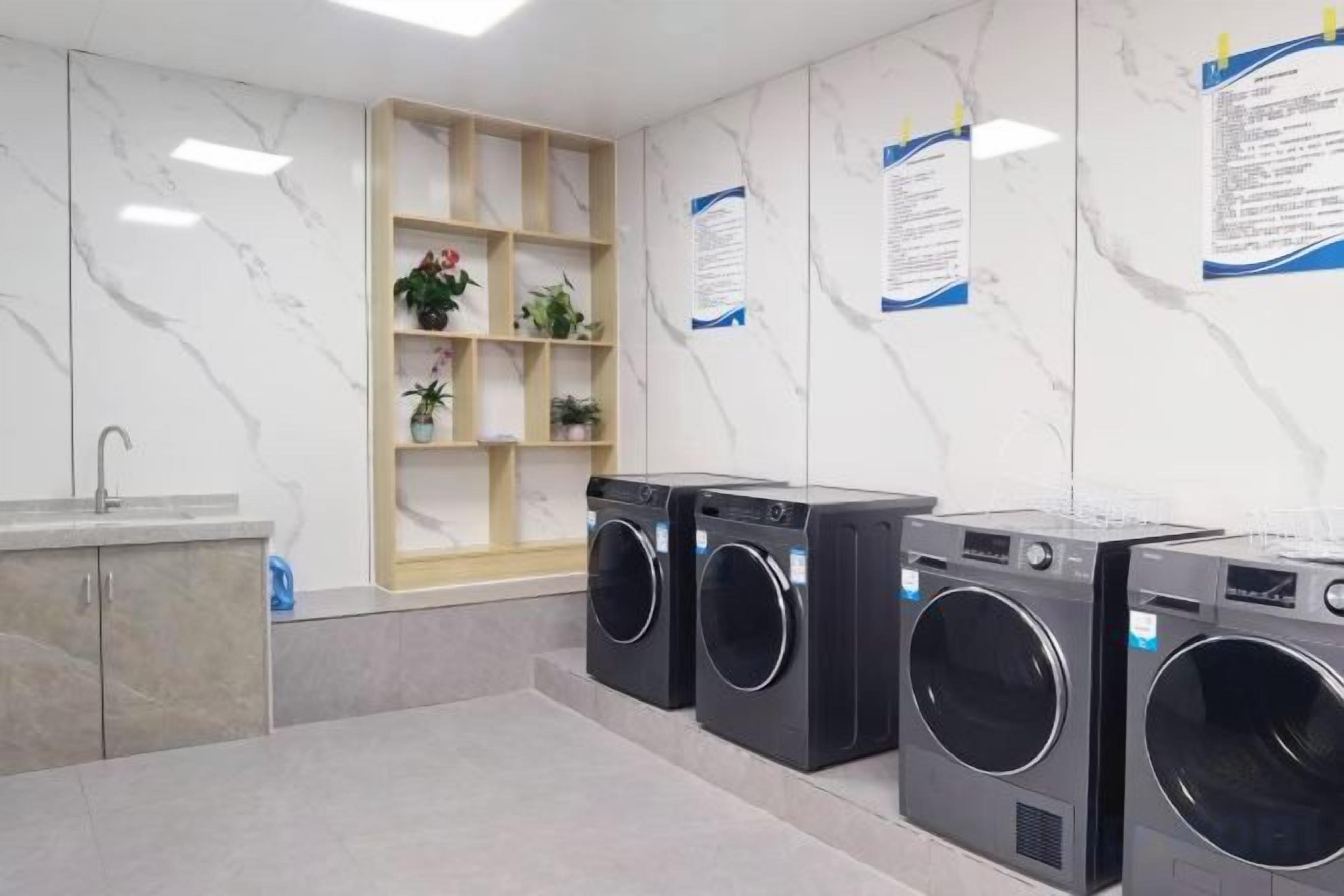 A laundry area with multiple washing machines, a sink, and a shelf with plants.