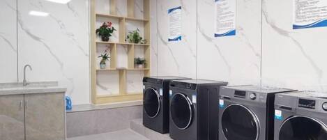 Un espace buanderie équipé de plusieurs machines à laver, d’un évier et d’une étagère où sont disposées des plantes.