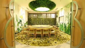 A conference room with a round table, chairs, a patterned carpet, and a green wall decoration.