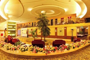 A hotel lobby with a curved reception desk, red seating, and a palm tree. - Fangzhou Hotel (Kunming)