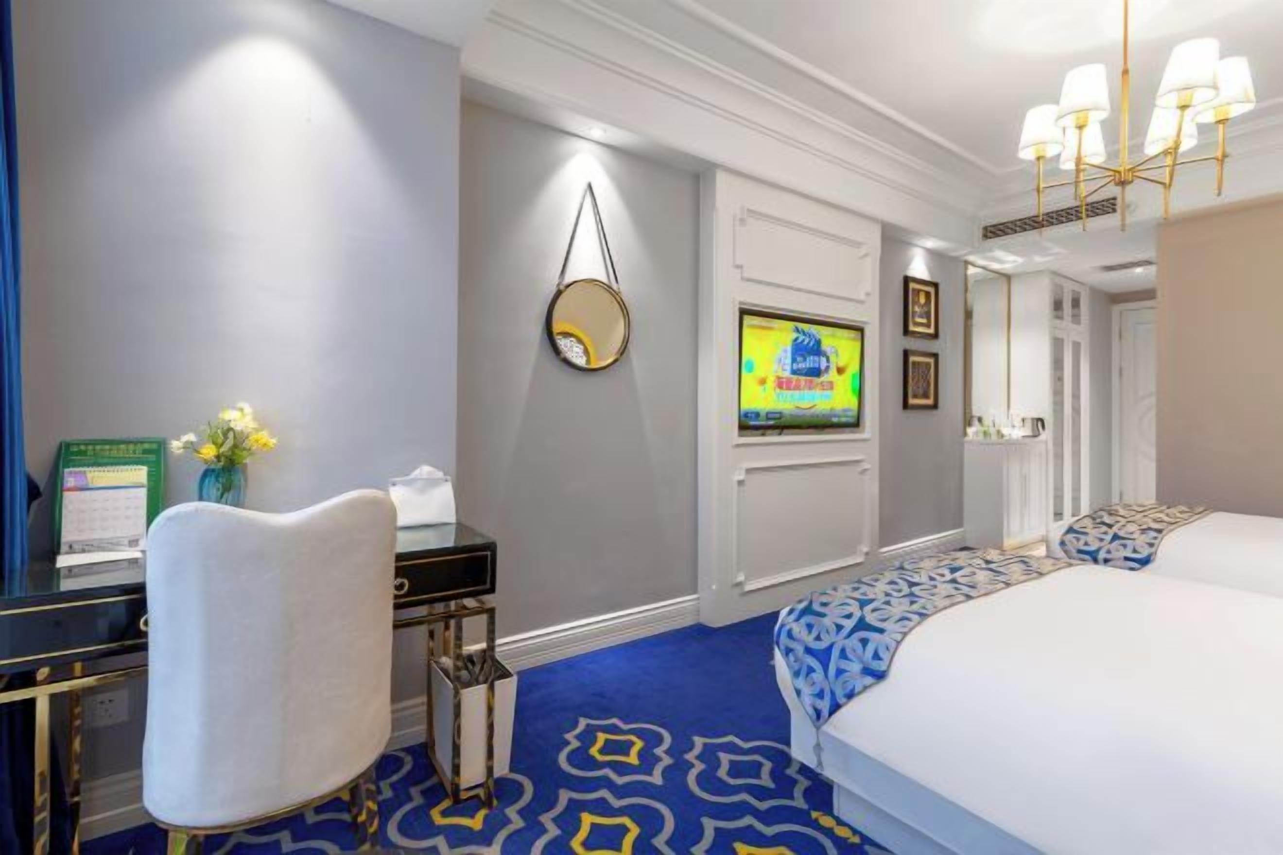 Ein Hotelzimmer mit einem Bett, einem Schreibtisch, einem Sessel, einem Fernseher, einem Spiegel und einem gemusterten Teppich.