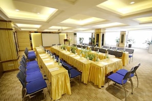 Une salle de conférence avec de longues tables, des chaises bleues et un tableau blanc.