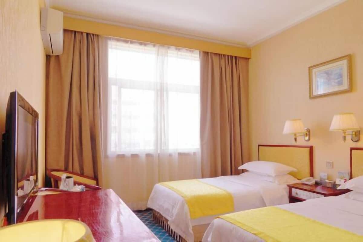 A hotel room with two beds, a desk, a chair, a TV, and a window with curtains.