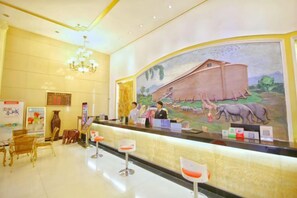 A hotel reception area with a large mural, a chandelier, and a counter with a receptionist. - Fangzhou Hotel (Kunming)
