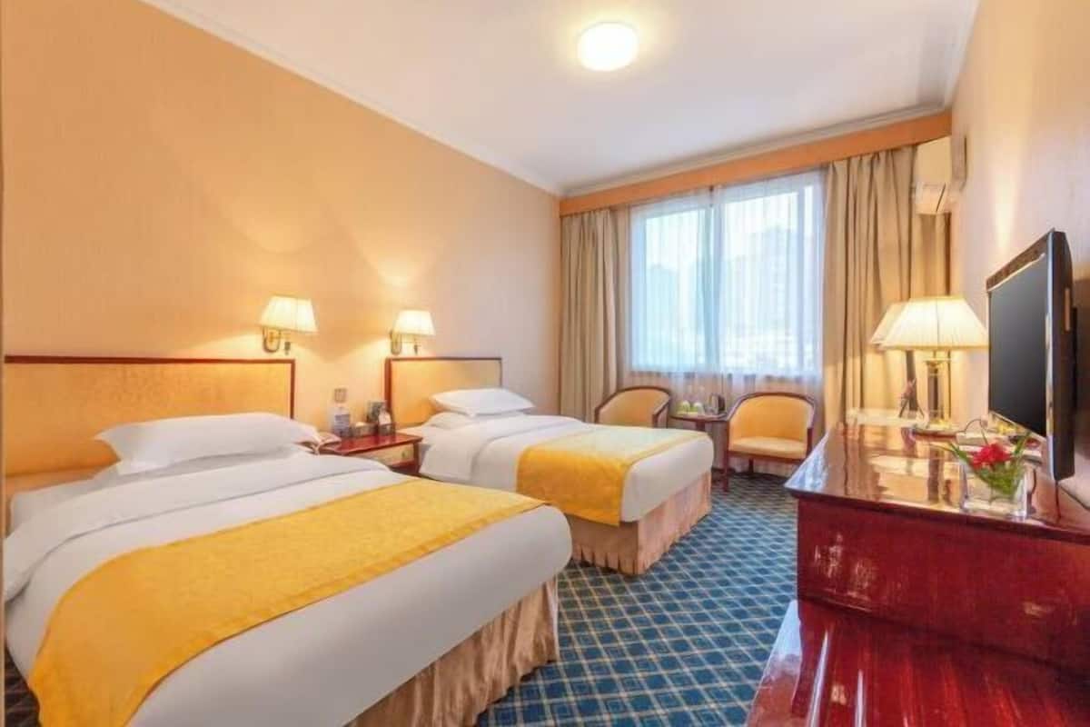 A hotel room with two beds, a desk, a chair, a TV, and a window with curtains.