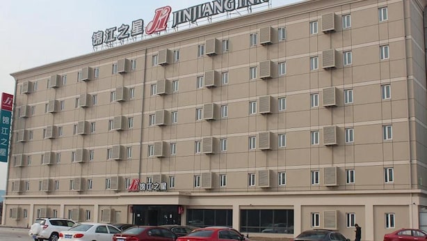 A multi-story hotel with a flat facade, multiple balconies, and a parking lot with several cars. - Jinjiang Inn (Beijing)