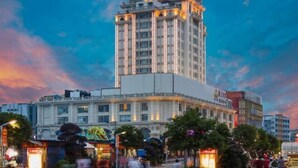 Un hotel de varios pisos con un cartel llamativo en la parte superior, rodeado de otros edificios y árboles.