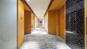 A hotel corridor with wooden walls, a patterned carpet, and a wall with circular designs. - Piaget Hotel (Anqing)