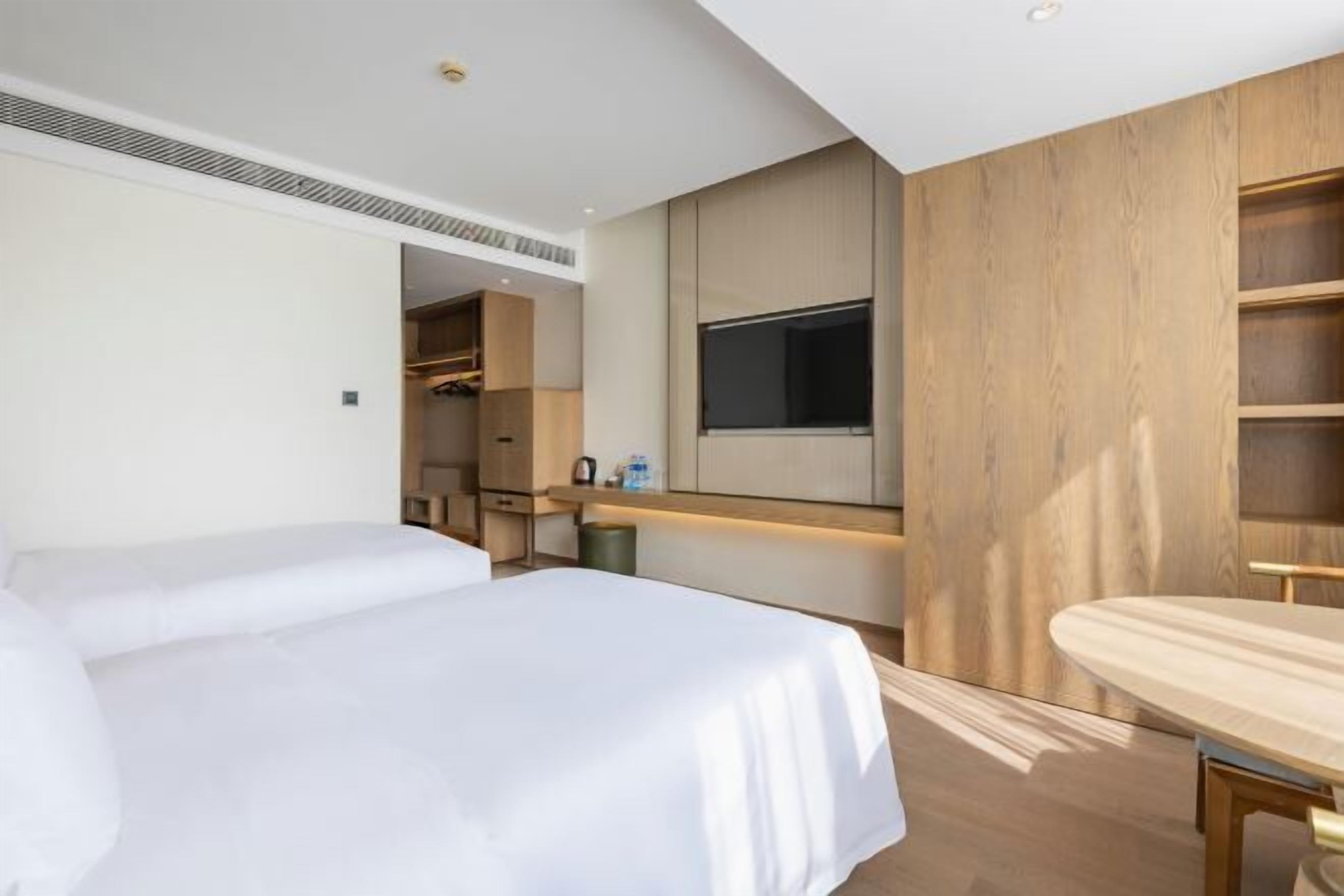 Una habitación de hotel moderna con dos camas, un escritorio de madera, un televisor montado en la pared y un vestidor.