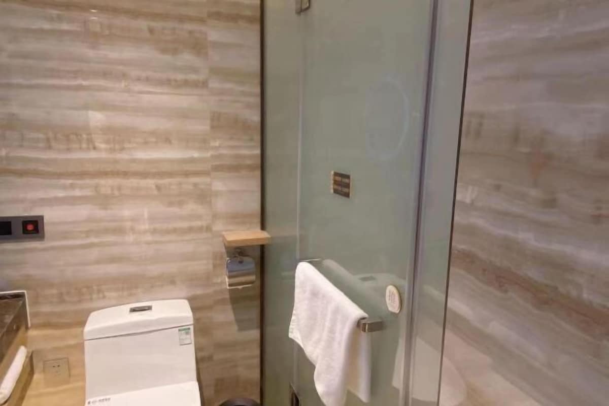 A bathroom with a marble wall, a glass shower enclosure, a towel hanging on a rack, and a white appliance.