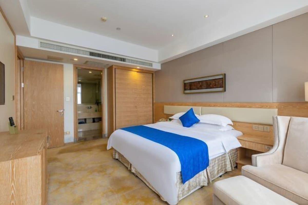 A hotel room with a large bed, a bedside table, a chair, and a wardrobe.