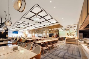 Un restaurant spacieux avec de hauts plafonds, des luminaires suspendus et différents types d’aménagements pour les places assises.