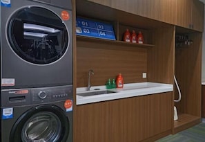 A compact laundry room with a washing machine, a sink, and a shelf with bottles.