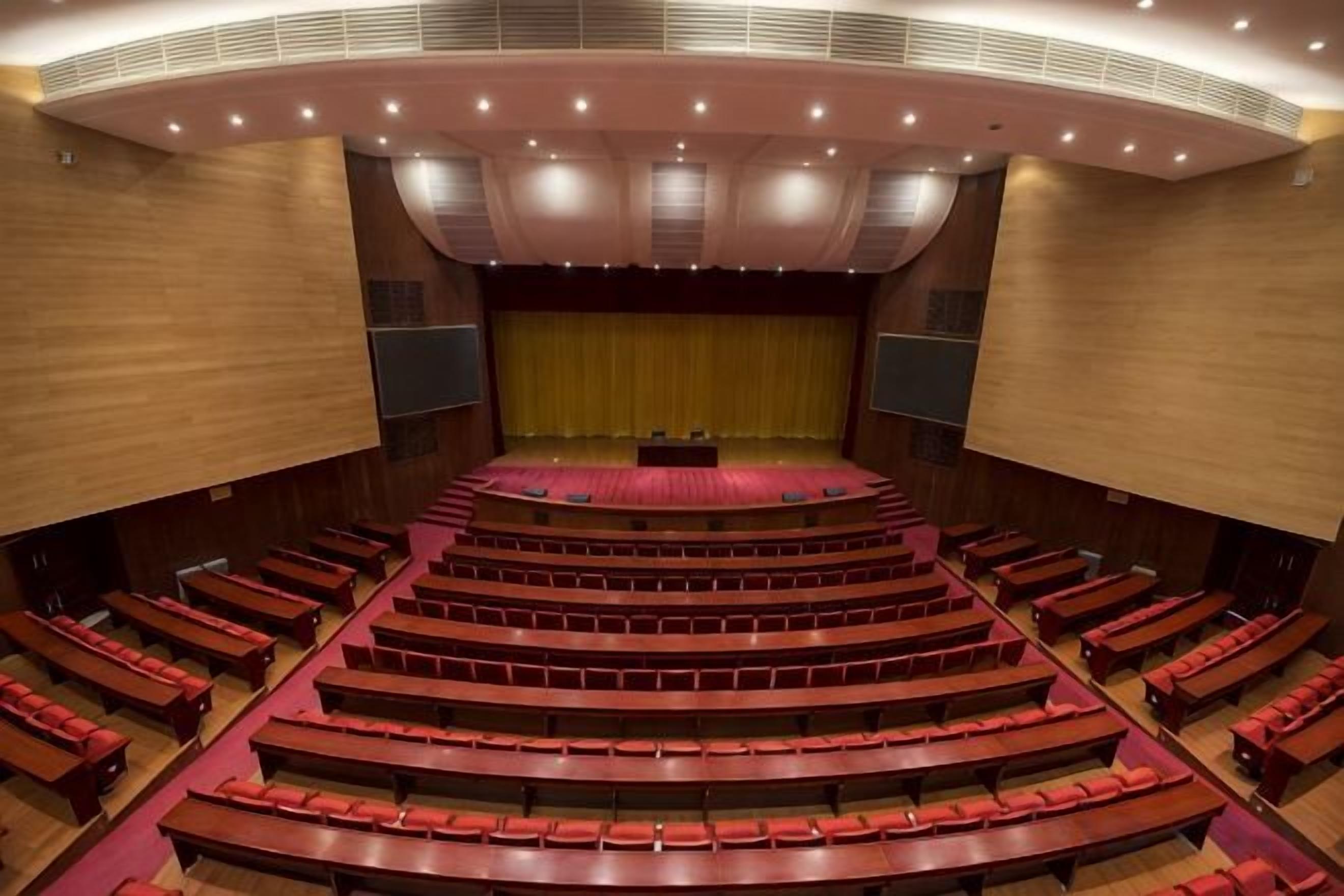 Un amplio auditorio con asientos escalonados, un escenario al frente y un techo curvo.