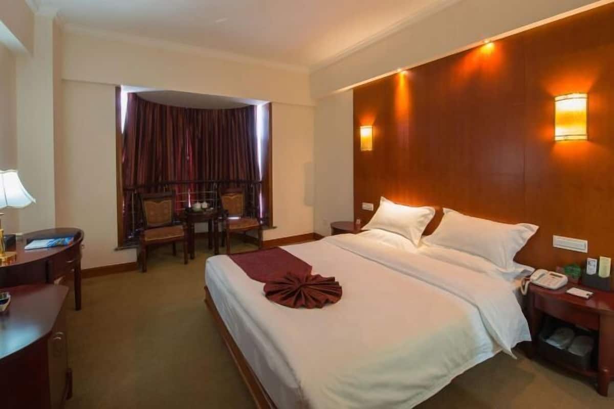 A hotel room with a large bed, a desk with a lamp, a chair, and a small table.