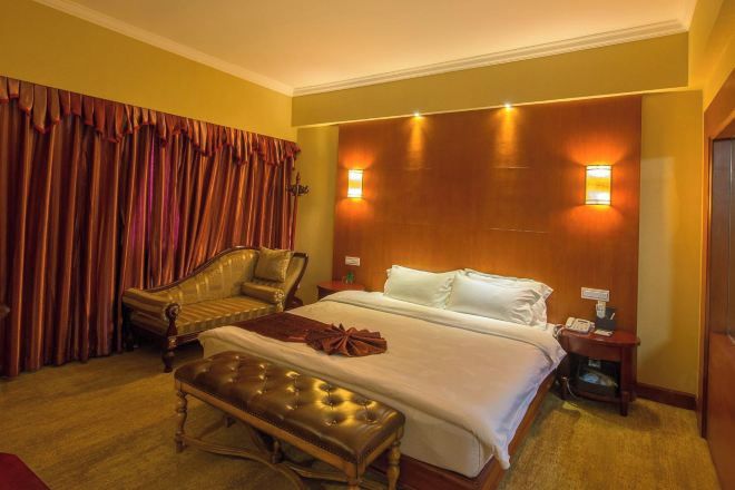 A hotel room with a large bed, a chaise lounge, a wooden headboard, and two bedside lamps.