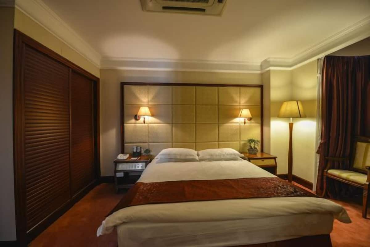 A hotel room with a large bed, two bedside lamps, a nightstand, a chair, and a window with curtains.