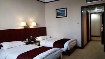 Una habitación de hotel con dos camas, una mesita de noche, una lámpara y un cuadro en la pared.