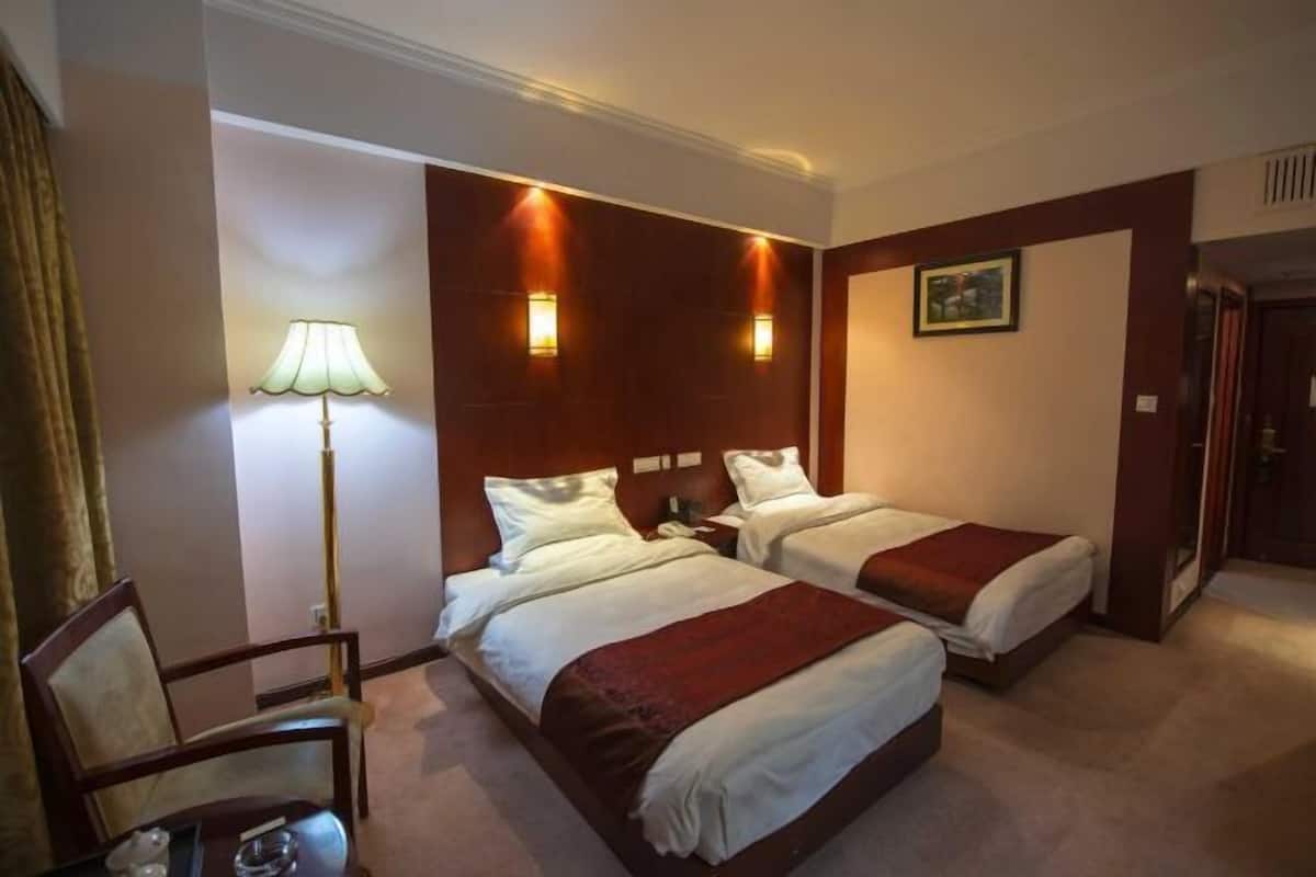A hotel room with two beds, a desk, a chair, a lamp, and a painting on the wall.