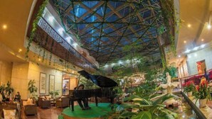 A spacious lobby with a grand piano, lush indoor plants, and a high ceiling with a geometric glass design. - Cangshan Hotel (DALI)