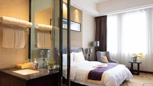 A hotel room with a large bed, a sitting area with a chair, a small table with a vase, and a large mirror. - Ruiyang Crown Hotel (Yining City)