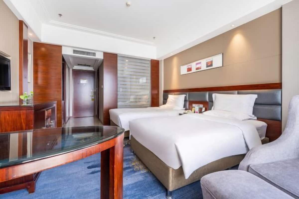 Hotellihuone, jossa on kaksi sänkyä, lasipöytä ja oleskelualue.