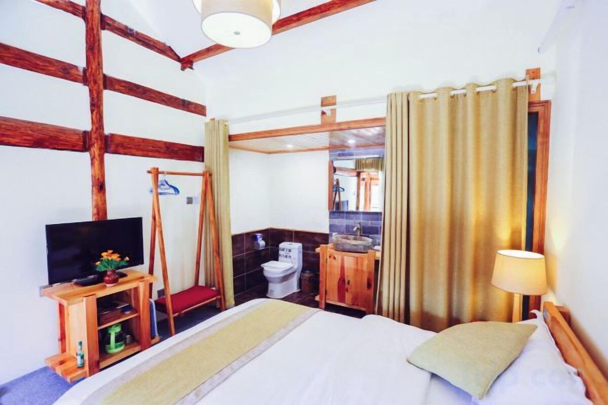 Habitación de hotel con cama, televisor, banca de madera, baño y cortinas.