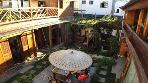 A courtyard with a wooden table and chairs under a large umbrella, surrounded by potted plants and a wooden fence. - Cabin 7 Inn (Dali)