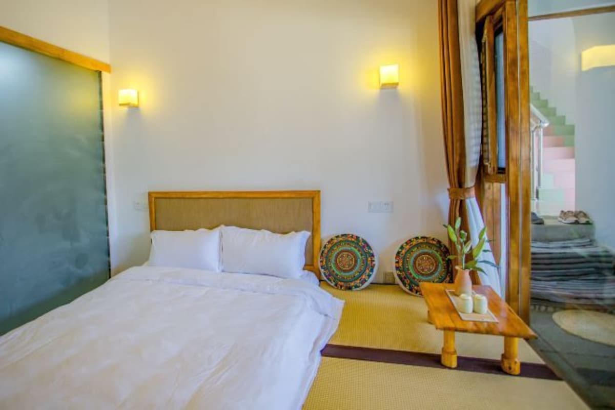 A hotel room with a bed, two wall-mounted lights, a small table with a plant, and decorative plates.