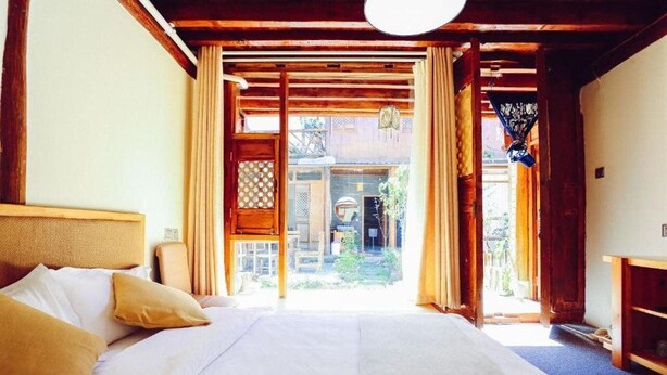 A room with a large bed, wooden beams, and a view of a garden. - Cabin 7 Inn (Dali)