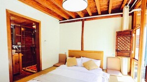A bedroom with a wooden ceiling, a bed with white bedding, a wooden headboard, and a small seating area. - Cabin 7 Inn (Dali)