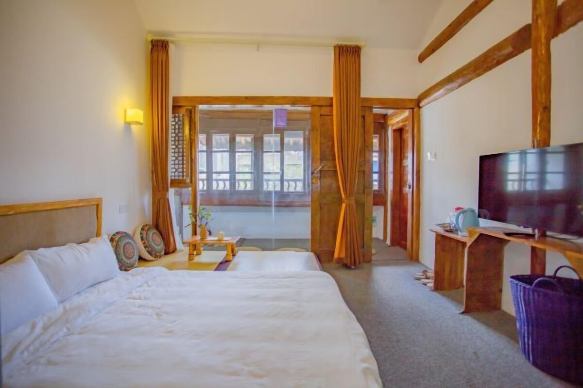 A hotel room with a large bed, a television, a desk with a chair, and a window with curtains.
