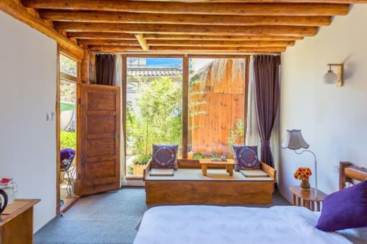 A cozy room with a wooden ceiling, a bed with a purple pillow, a small table, and a bench with cushions.