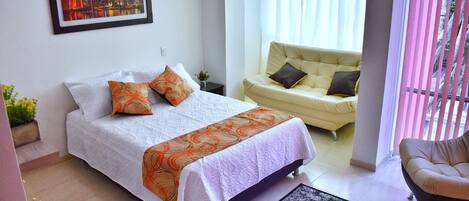 A bedroom with a bed, a sofa, and a window with curtains.