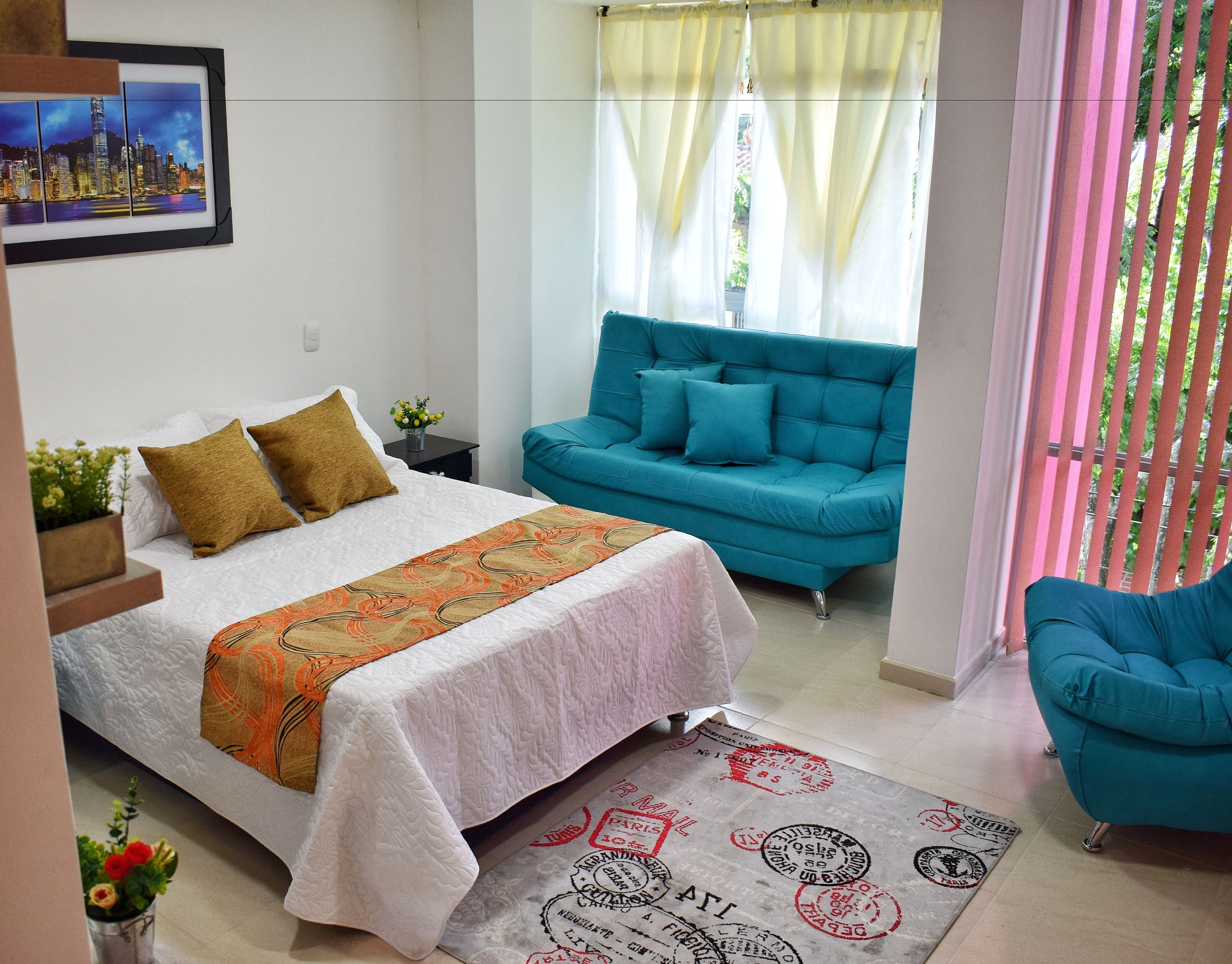 A bedroom with a bed, a sofa, a chair, and a window with curtains.
