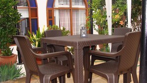 A patio with a table and chairs, surrounded by potted plants and a building with arched windows. - Villa Pepita Real (Villa de Leyva)