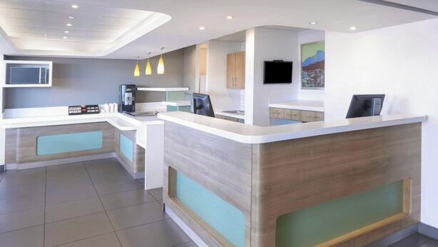 A modern hotel lobby with a reception desk, seating area, and a kitchen in the background. - SUN1 Milnerton (Cape Town)