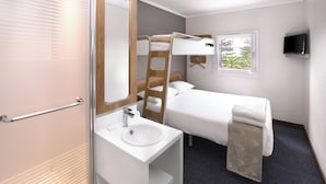 Ein modernes Hotelzimmer mit Stockbett, einem Fernseher am Nachttisch, einem großen Spiegel und einem Fenster mit Blick auf Bäume.