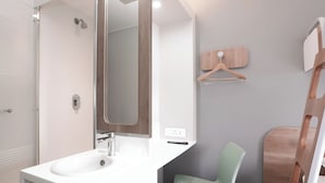 Ein modernes Badezimmer mit einem weißen Waschbecken, einem Spiegel, einer Dusche und einem Holzstuhl.