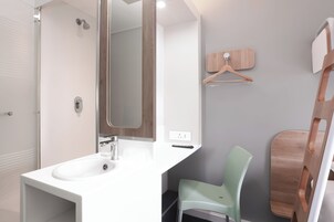 Un baño moderno con lavamanos blanco, un espejo, ducha y una silla de madera.