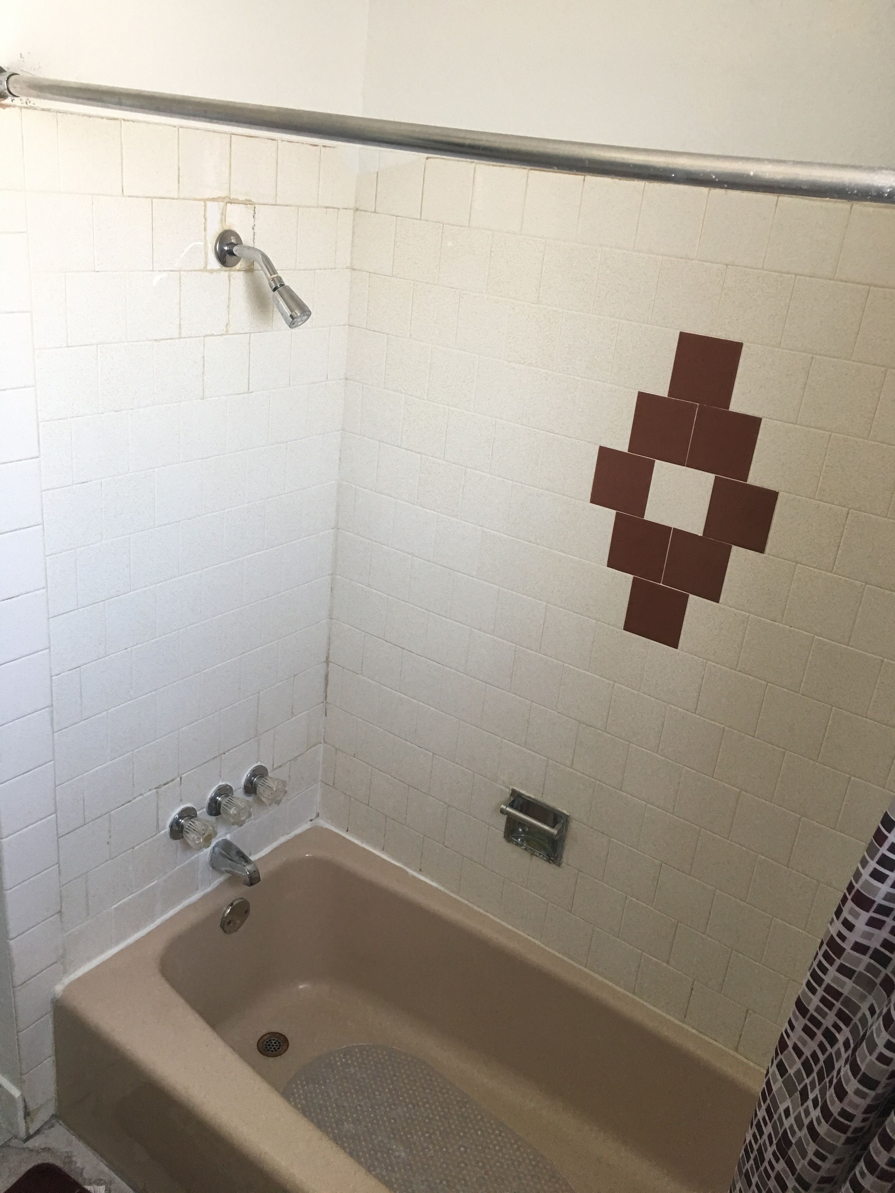A bathroom with a bathtub, white and brown tiles, and a shower area.