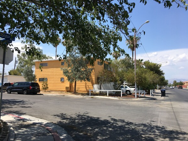 Um edifício amarelo com cerca branca, rua e carros estacionados.