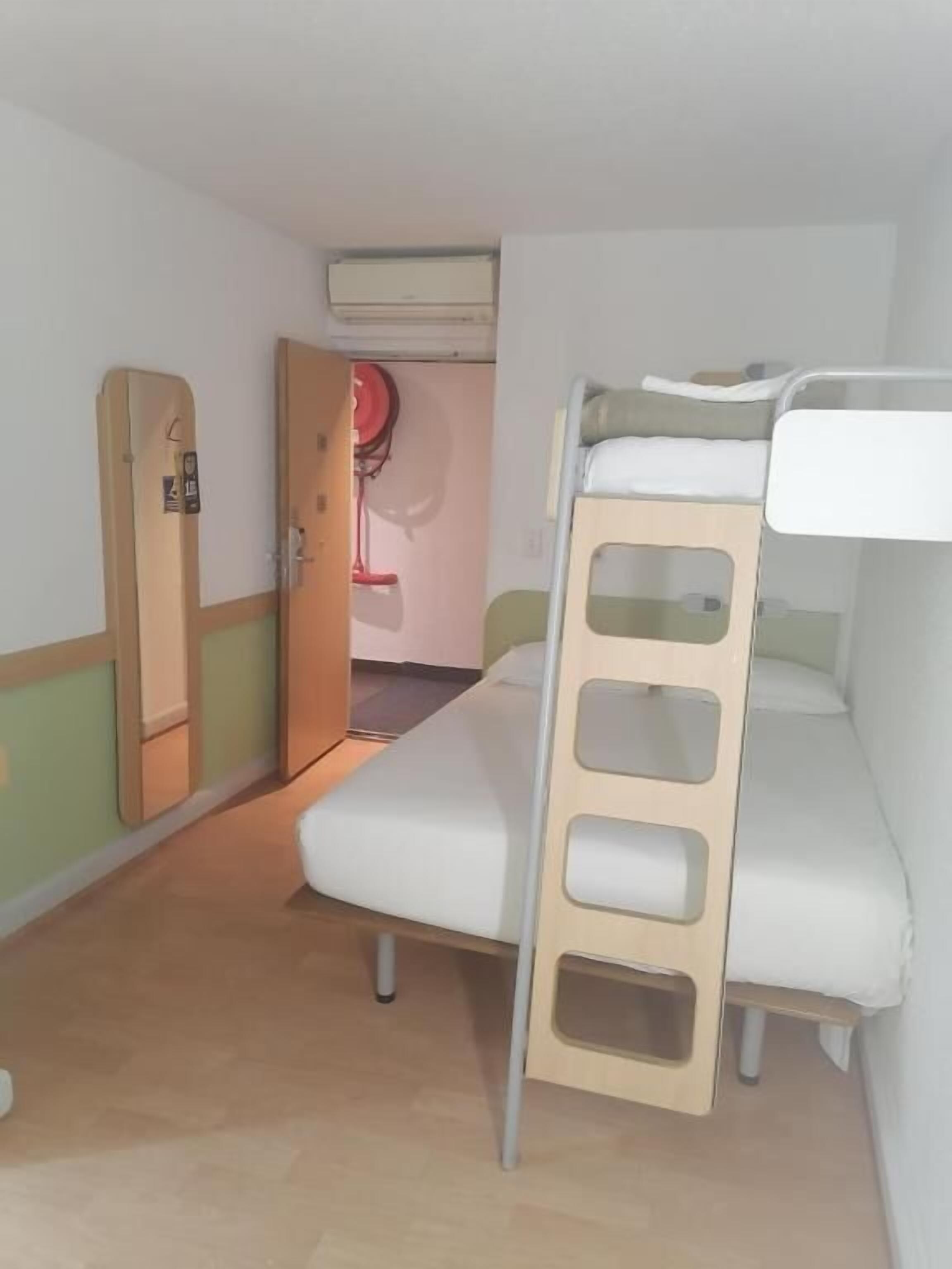 A bunk bed room with a door, an air conditioning unit, and a small table.