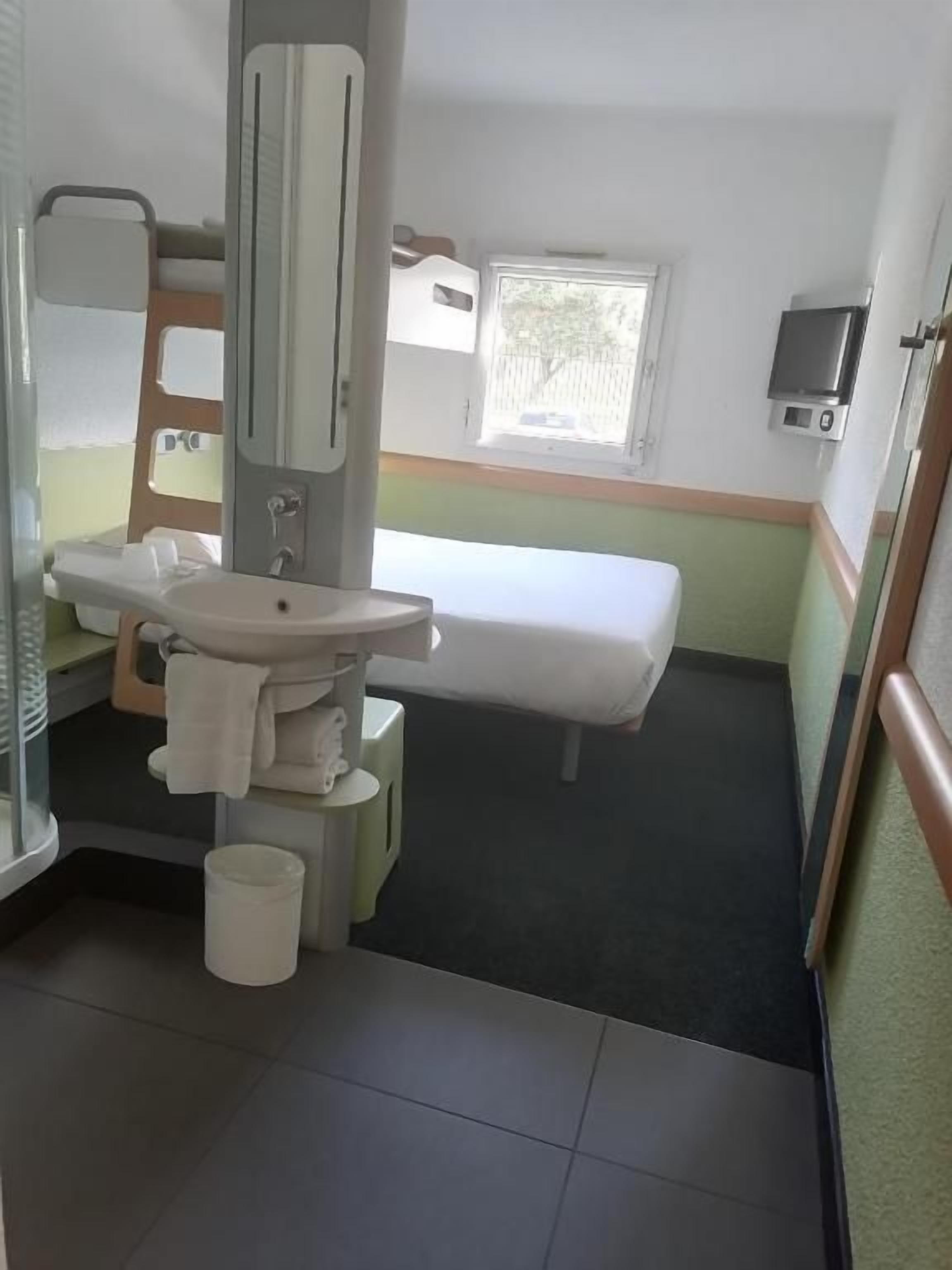 A small, compact hotel room with a single bed, a sink, and a mirror.