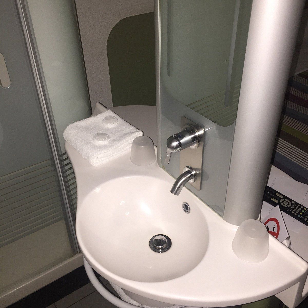 A bathroom with a white sink, a glass shower enclosure, and a towel dispenser.